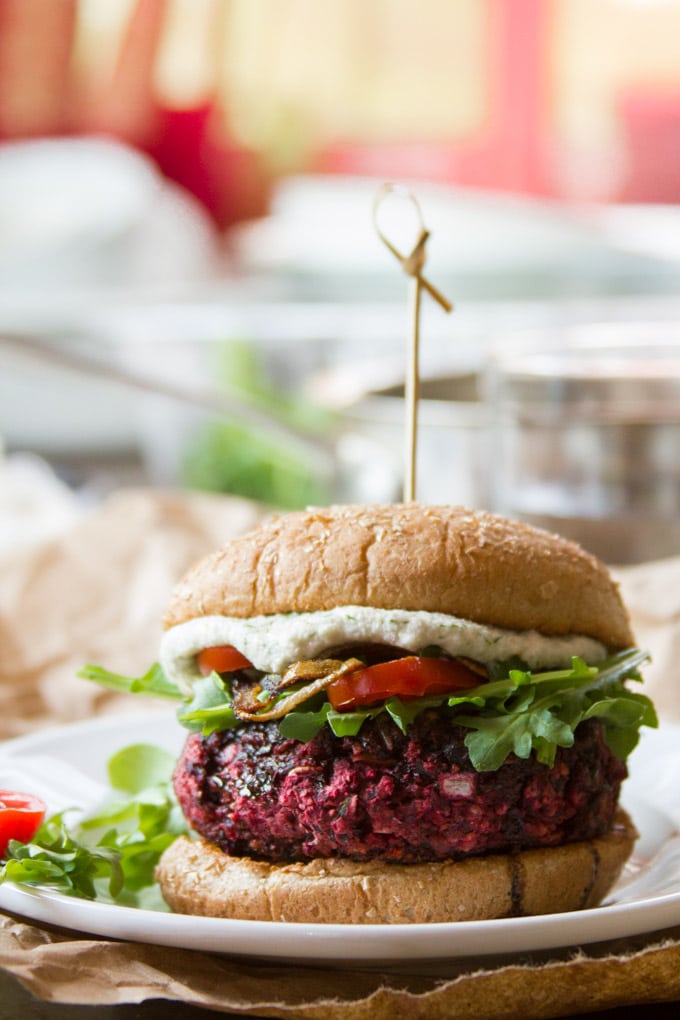 Close Up of a Beet Burger on a Plate Topped with Arugula, Tomatoes, and Cashew Cheese.