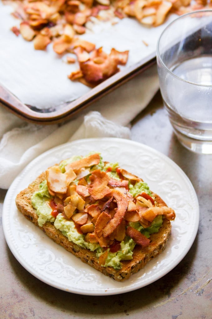 Slice of Avocado Toast on a Plate Topped with Coconut Bacon.