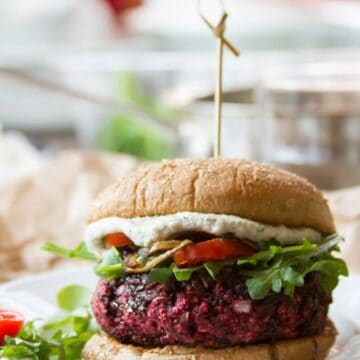 Close Up of a Beet Burger on a Plate Topped with Arugula, Tomatoes, and Cashew Cheese