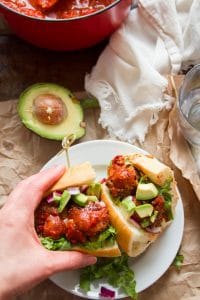 Hand Grabbing Half of a Vegan Mexican Meatball Sub From a Plate