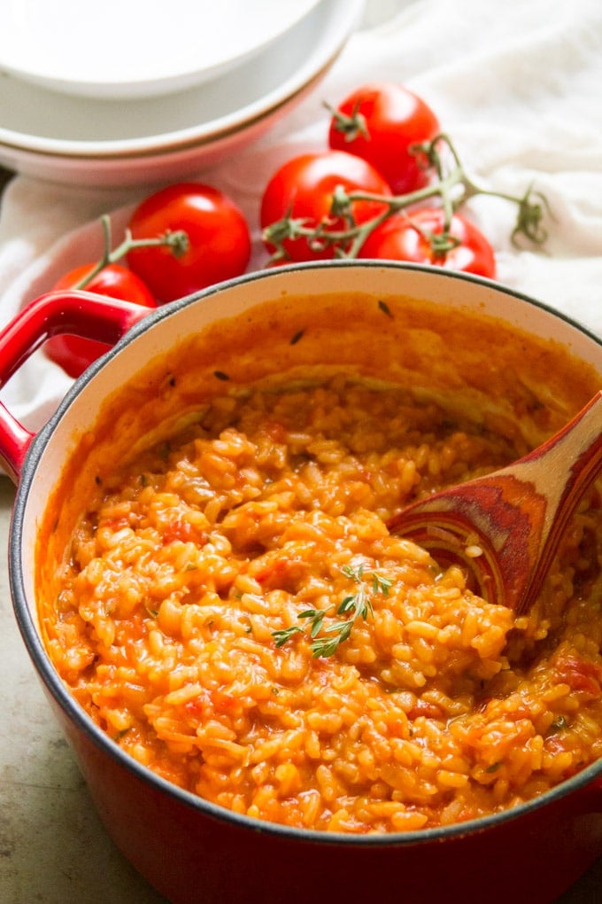 Pot of Caramelized Onion and Tomato Risotto with a Stack of Bowls and Fresh Tomatoes in the Background