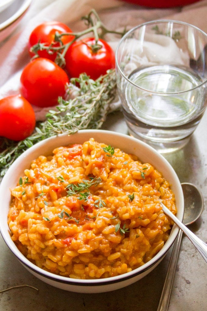 Bowl of Caramelized Onion & Tomato Risotto With Water Glass, a Bunch of Thyme and Fresh Tomatoes in the Background