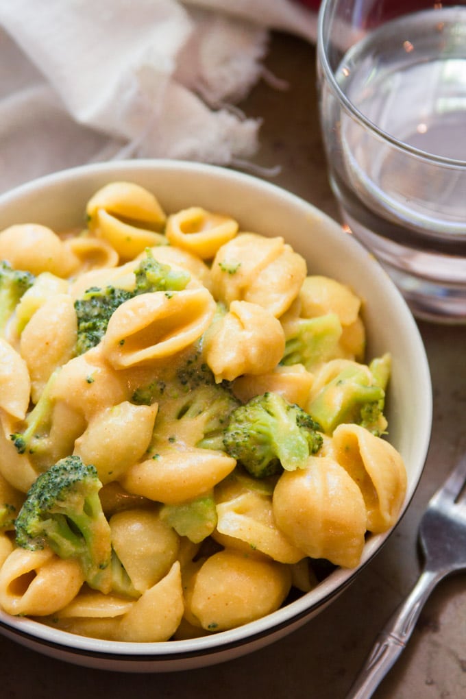 Close Up of a Bowl of Creamy Coconut Mac & Cheese with Broccoli with Drinking Glass and Fork