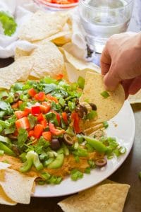 Hand Dipping a Chip into a Plate of Cheesy Vegan Taco Dip
