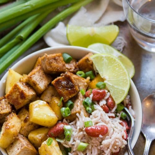 Jamaican Jerk Tofu Bowl with Fork, Lime Slices, Drinking Glass, and Scallions in the Background