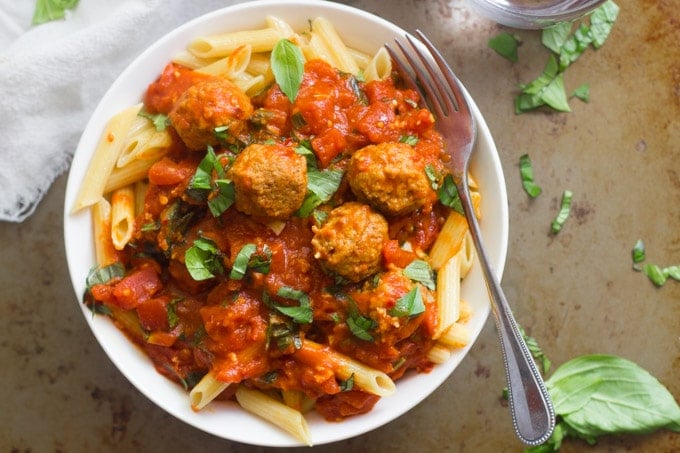 Overhead View of a Bowl of Penne Arrabbiata Topped with Basil and Lentil Meatballs