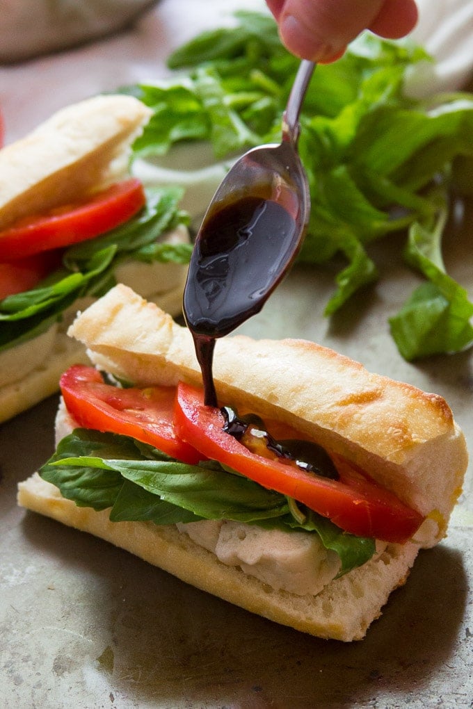 Spoon Drizzling Balsamic Reduction on a Vegan Caprese Sandwich