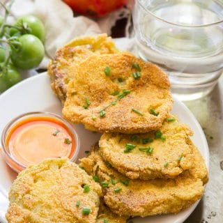 Vegan Fried Green Tomatoes on a Plate with Fresh Tomatoes and Water Glass in the Background