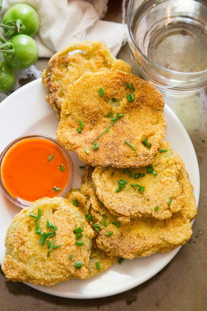 Overhead View of Vegan Fried Green Tomatoes on a Plate with Hot Sauce and Drinking Glass