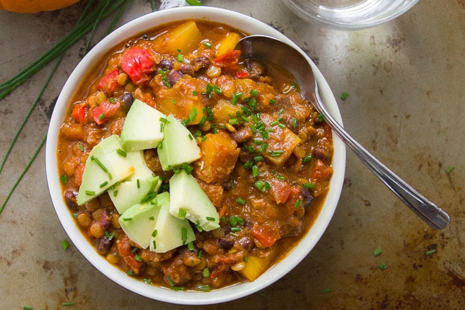 Overhead View of a Bowl of Vegan Triple Pumpkin Chili with Spoon and Avocado Slices