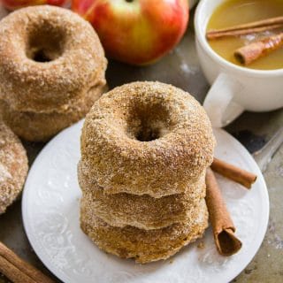 Stack of Vegan Apple Cider Doughnuts on a Plate with Cinnamon Sticks
