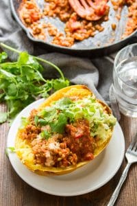 Taco Stuffed Spaghetti Squash on a Plate with Drinking Glass and Skillet in the Background