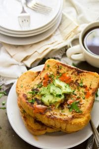 Savory Vegan French Toast on a Plate with a Stack of Dishes and Coffee Cup in the Background