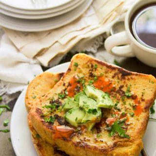 Savory Vegan French Toast on a Plate with a Stack of Dishes and Coffee Cup in the Background