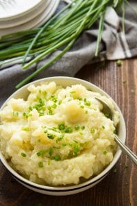 Truffled Mashed Potatoes in a Bowl with Plates and a Bunch of Chives in the Background