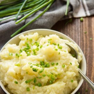 Truffled Mashed Potatoes in a Bowl with Plates and a Bunch of Chives in the Background