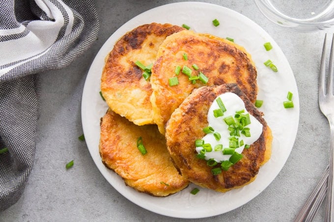 Overhead View of Cheesy Vegan Mashed Potato Pancakes on a Plate Topped with Vegan Yogurt and Chives