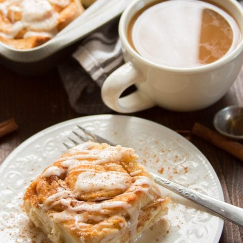 Vegan Cinnamon Roll on a Plate with Fork and Coffee Cup in the Background