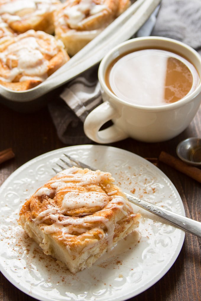Vegan Cinnamon Roll on a Plate with Fork and Coffee Cup in the Background