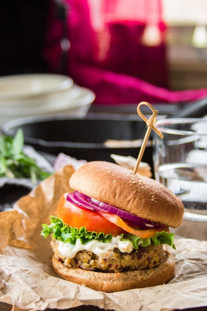 Greek Chickpea Burger on a Bun with Dishes, Water Glass and Skillet in the Background