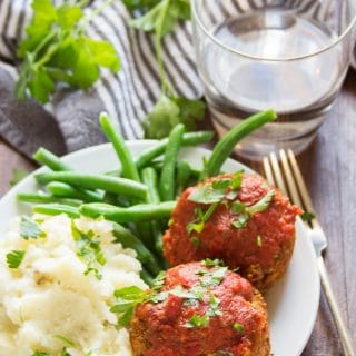 Plate Filled with Italian-Style Vegan Meatloaf Muffins, Mashed Potatoes, and Green Beans, with Napkin and Water Glass in the Background