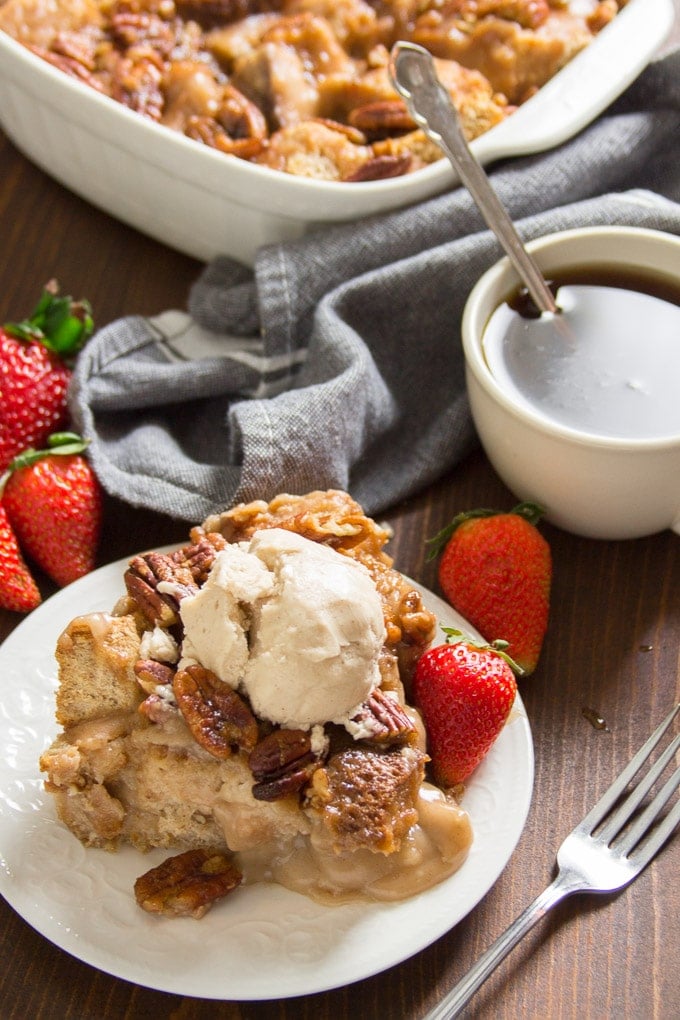 Slice of Maple Pecan Vegan Bread Pudding Topped with an Ice Cream Scoop, with Coffee Cup and Strawberries in the Background