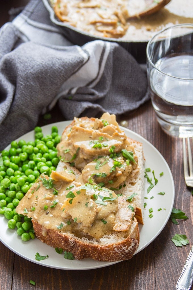 Hot Open-Faced Vegan Turkey & Gravy Sandwich and Peas on a Plate with Napkin and Water Glass in the Background