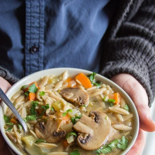 Hands Holding a Bowl of Mushroom Lemon Orzo Soup with Spoon