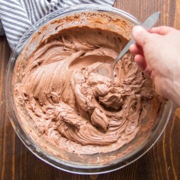 Hand scooping Vegan Chocolate Buttercream Frosting from a bowl with spoon.