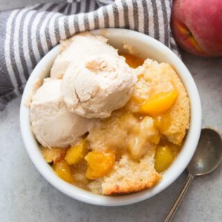 Bowl of Vegan Peach Cobbler and Vegan Vanilla Ice Cream with a Spoon on the Side