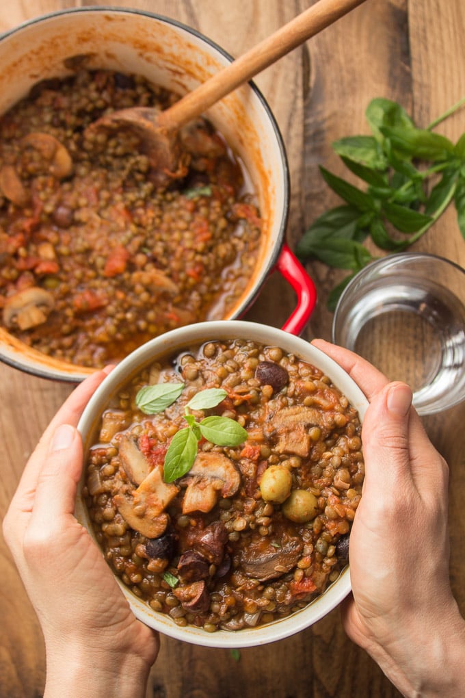 Pair of Hands Holding a Bowl of French Lentil Stew Over a Table