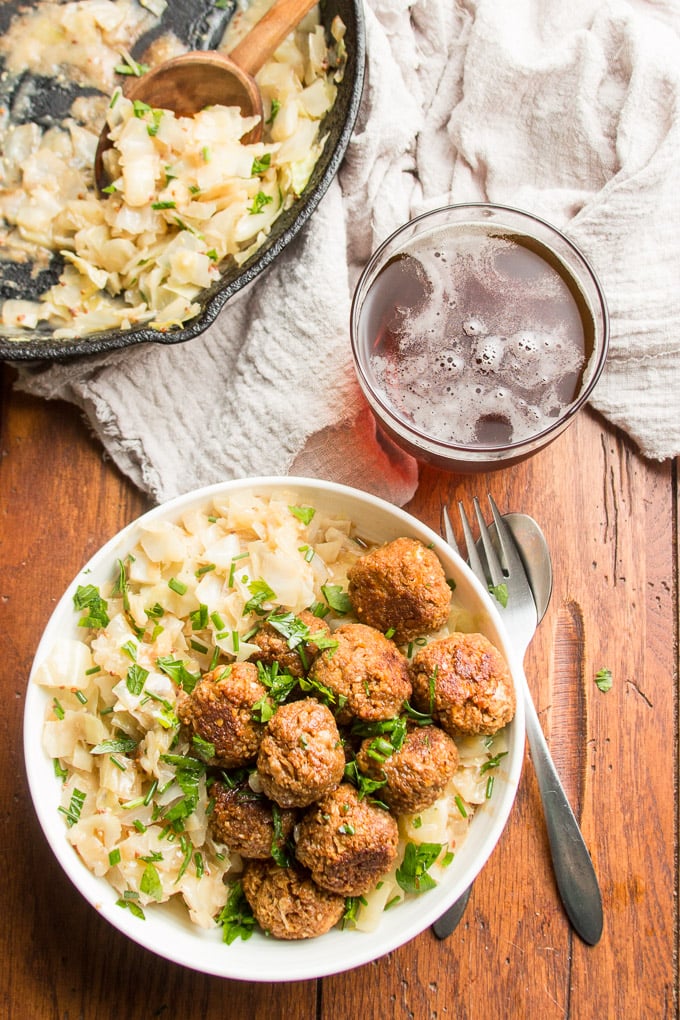Table Set with Bowl of Vegan German Meatballs & Cabbage, Silverware, Napkin, Glass of Beer and a Skillet of Cabbage