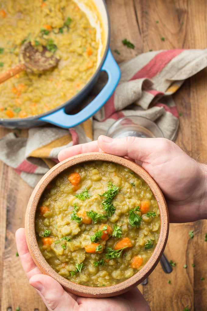 Pair of Hands Holding a Bowl of Vegetarian Split Pea Soup Over a Table