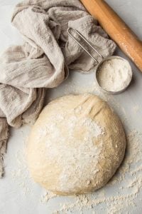 Ball of Whole Wheat Pizza Dough with Measuring Cup, Rolling Pin and Tea Towel