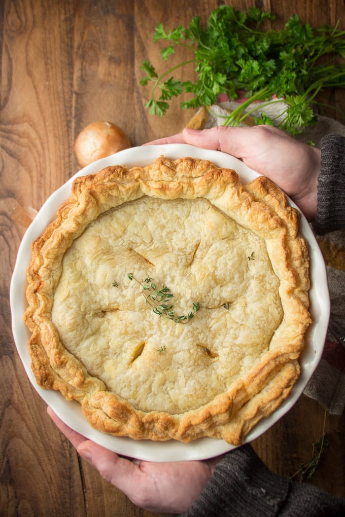 Pair of Hands Holding a Vegan Cheese & Onion Pie Over a Table