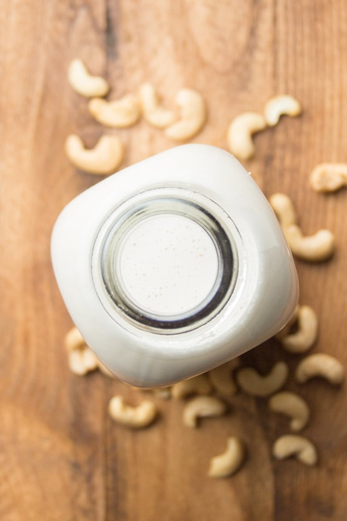 Bottle of Cashew Milk Surrounded By Cashews on a Wooden Surface