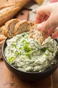 Hand Dipping Bread into a Bowl of Vegan Spinach Dip