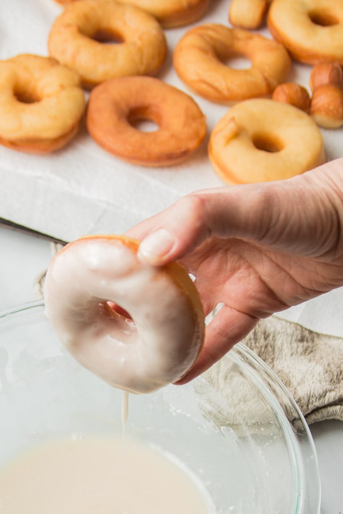 Hand Dipping a Vegan Doughnut into a Bowl of Glaze