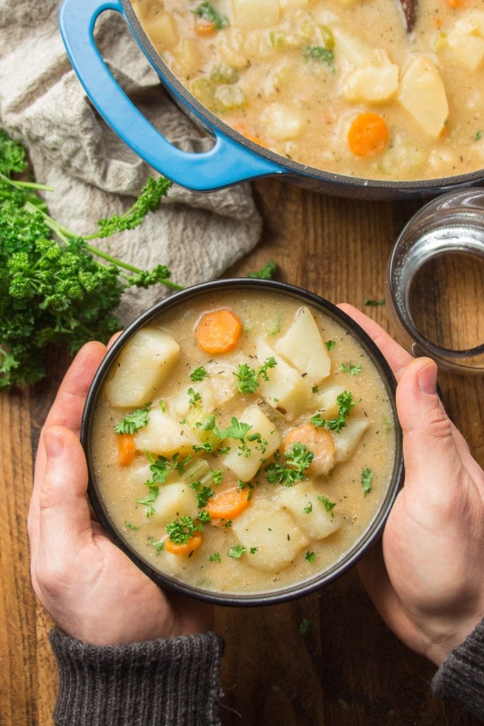 Pair of Hands Holding a Bowl of Vegan Potato Soup Over a Table
