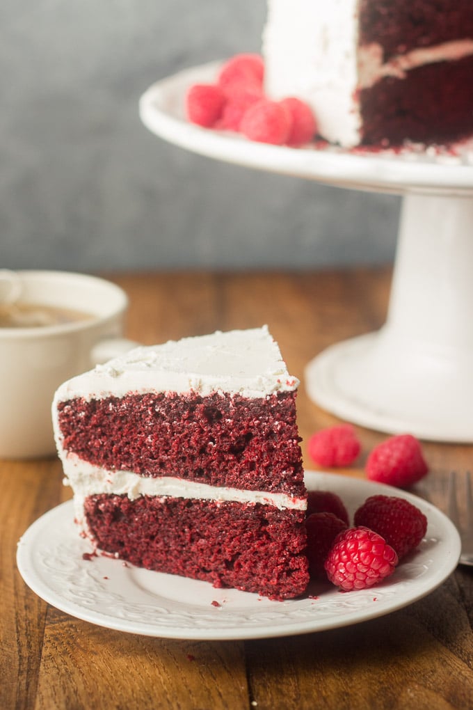 Vegan Red Velvet Cake on a Plate with Tea Cup and Cake Dish in the Background