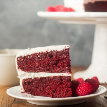 Slice of Vegan Red Velvet Cake on a plate with raspberries.