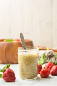 Jar of Poppy Seed Dressing with Strawberries and Wooden Salad Bowl in the Background