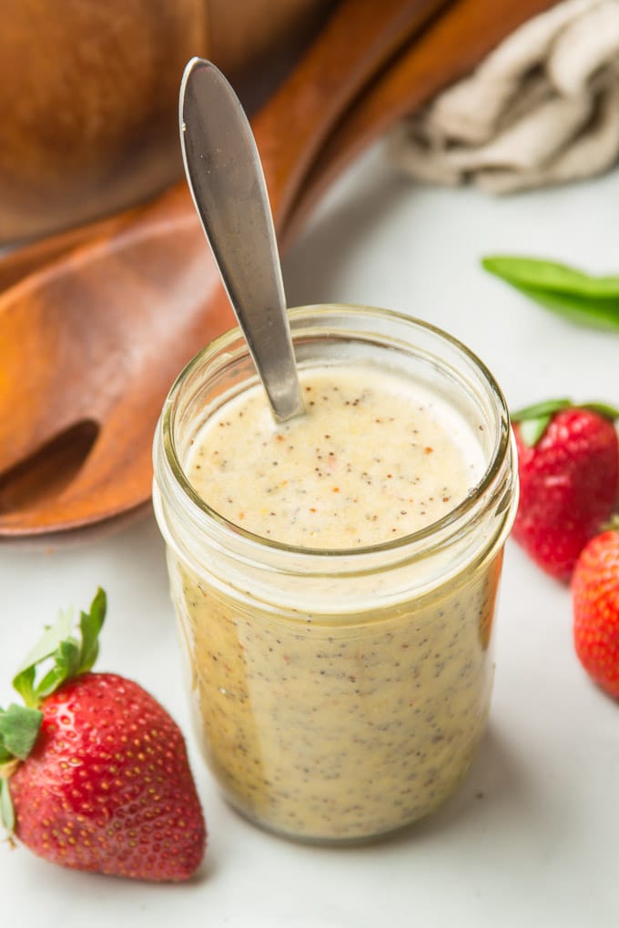 Jar of Poppy Seed Dressing Surrounded By Strawberries and Two Wooden Salad Spoons