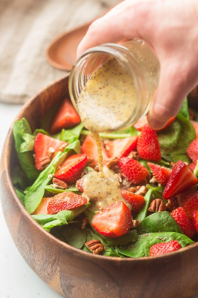 Hand Pouring Poppy Seed Dressing Over a Strawberry Spinach Salad
