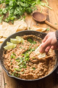 Hand Dipping a Chip into a Skillet of Vegan Refried Beans