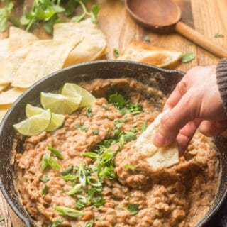 Hand Dipping a Chip into a Skillet of Vegan Refried Beans