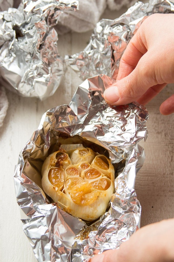 Hand Opening a Foil Wrapped Bulb of Roasted Garlic