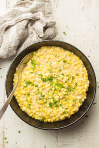 Vegan Creamed Corn in a Black Bowl on White Wooden Surface with Spoon