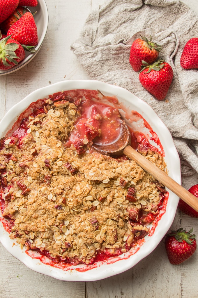 Vegan Strawberry Crisp in a Baking Dish with Scoop Removed By Wooden Spoon
