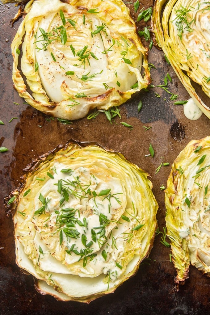 Overhead View of Cabbage Steaks Topped with Dressing and Herbs on a Baking Sheet